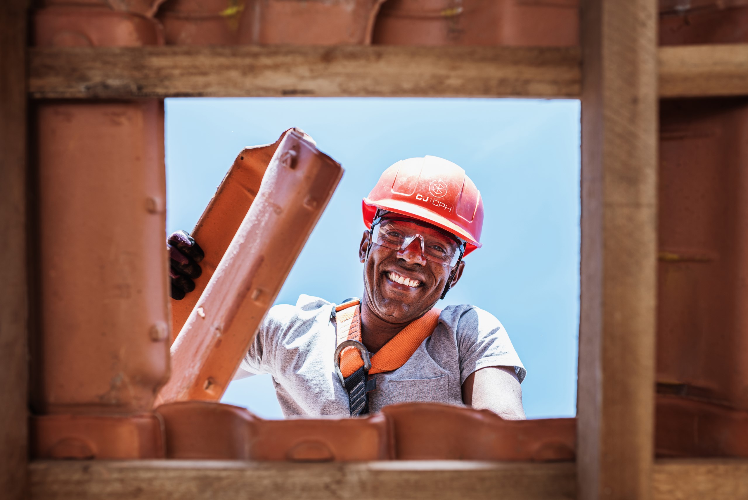 Latin worker installing yellow ceramic roofing tiles mounted on wooden boards covering residential building roof under construction.